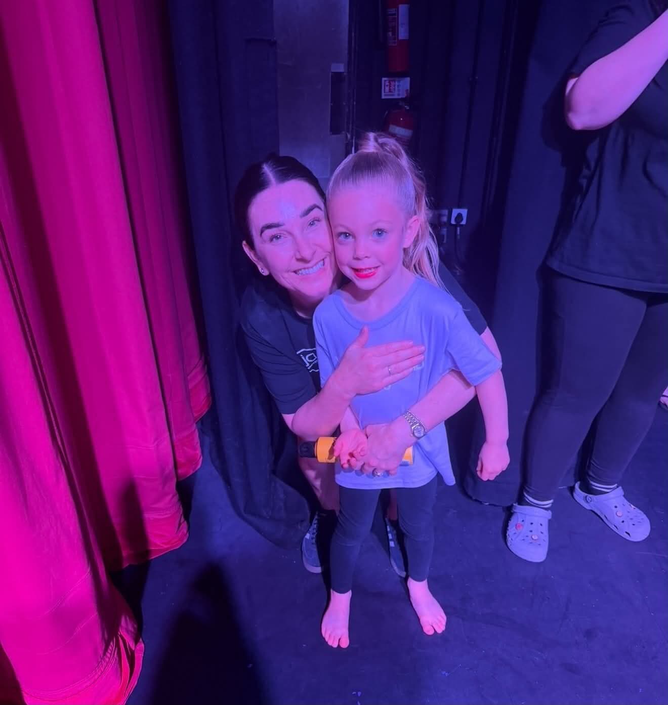 Teacher and tiny dancer cuddled by the backstage curtain